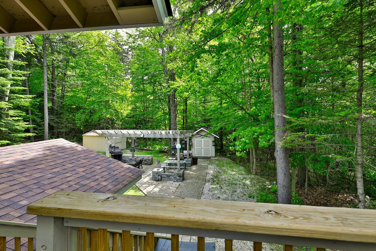 An expansive deck area framed by a wooden railing and featuring a pergola with outdoor seating, surrounded by lush trees. The tranquil setting offers a peaceful spot for socializing or relaxing, extending the evening outdoors.