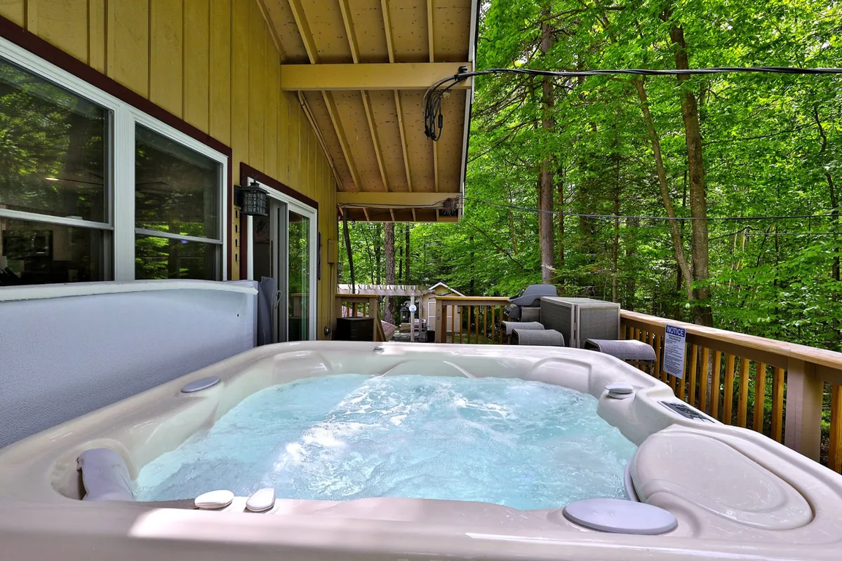 An outdoor hot tub bubbles invitingly on a wooden deck, surrounded by lush greenery. The space is ideal for relaxing sore muscles after a day on the slopes, with plenty of room for socializing and unwinding in nature.