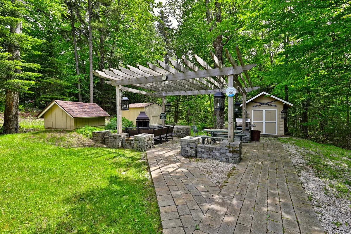 An inviting outdoor space featuring a pergola with stone seating, a grill, a picnic table, and a dedicated shed nestled amidst lush greenery. The shed is ideal for safely storing bikes or other adventure gear, while the picnic area and grill suggest al fresco dining and outdoor gatherings.