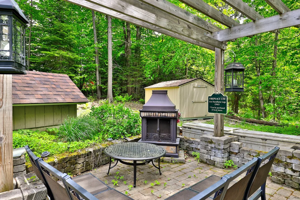 An inviting outdoor living area with a fireplace, comfortable seating, and a pergola set among landscaped greenery. The space is ideal for gathering in the evenings, savoring the fresh air, and reflecting on local adventures.