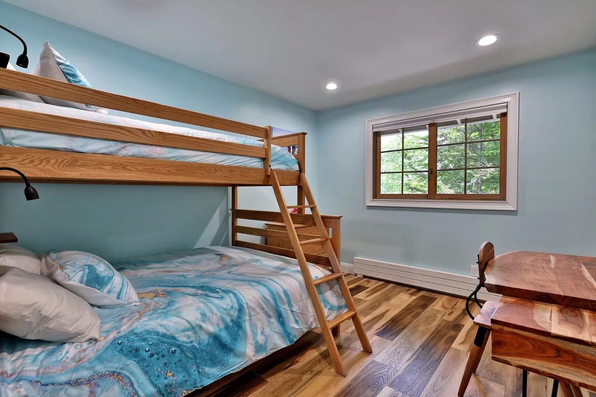 A playful bedroom with bunk beds adorned in colorful bedding and a sturdy wooden desk. The space exudes a sense of fun and relaxation, ideal for kids or groups of friends.