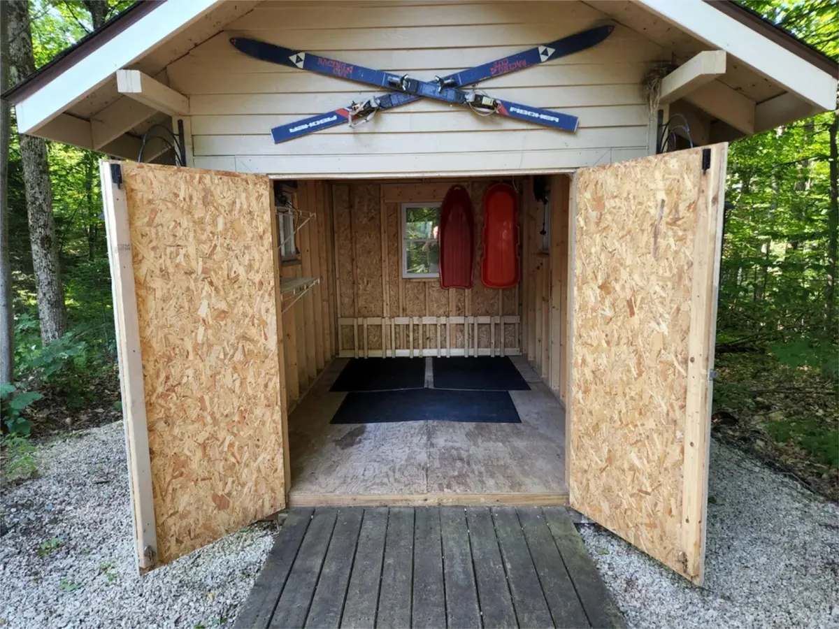 A storage area filled with ski equipment and sleds, with open doors ready for guests to grab their gear. The playful and practical space is designed to support winter adventures, ensuring easy transitions from outdoor activities to indoor relaxation.