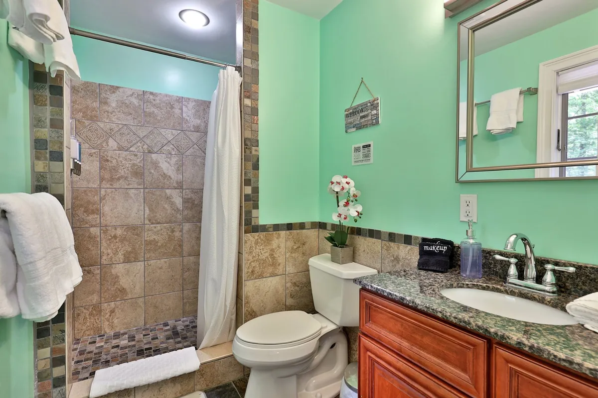 A modern bathroom featuring a walk-in shower, a sleek vanity with a sink, decorative wall decor, and a touch of greenery with a potted plant. Soft lighting creates a spa-like retreat.