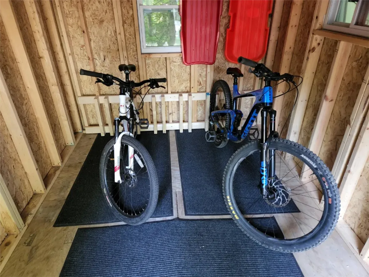 A practical storage area featuring two bicycles and red sleds placed on carpeted flooring, suggesting active outdoor use. The space is designed for easy access to gear, supporting both summer and winter adventures.