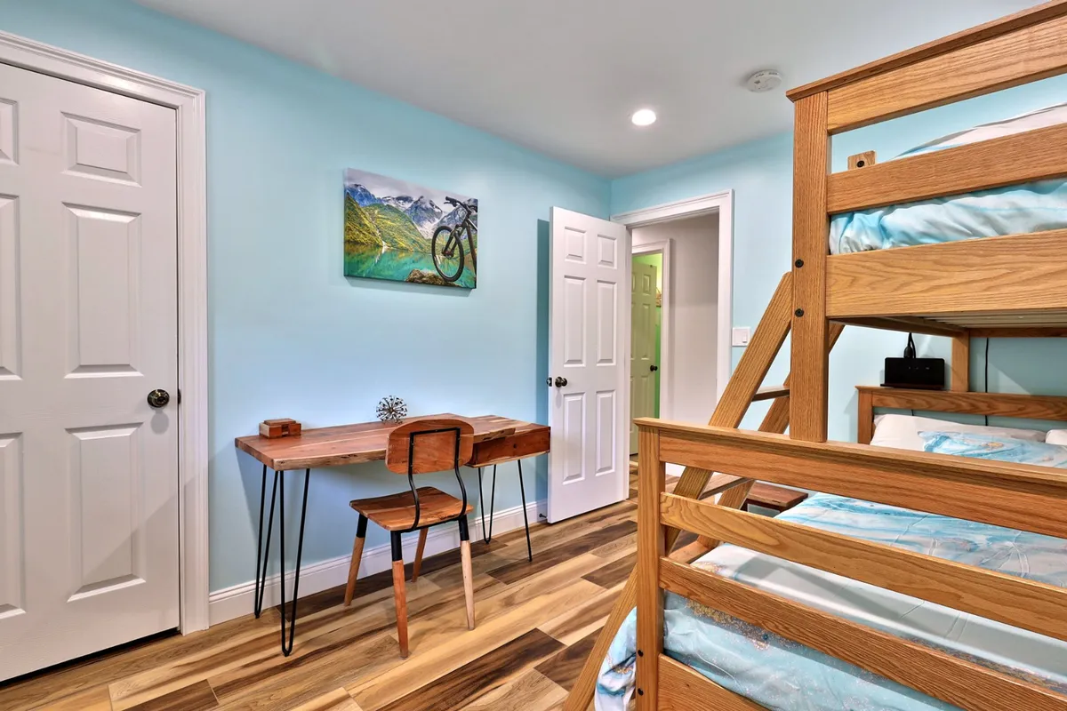 A comfortable bedroom with two sets of bunk beds, a wooden desk, and mountain bike artwork, creating a relaxed and versatile environment for sleep, study, and socializing.