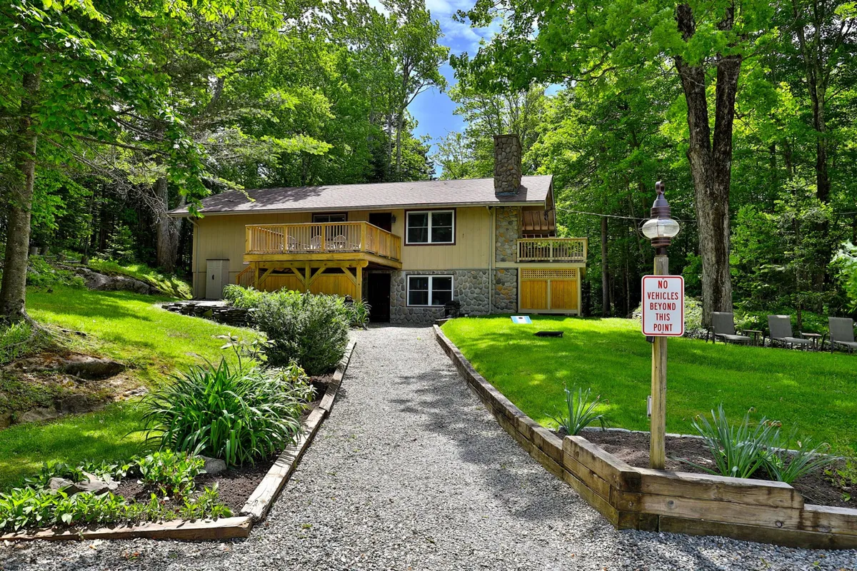A view of the home's front entrance with a spacious deck area and landscaped garden, set against a backdrop of mature trees. The scene exudes a sense of privacy and tranquility, inviting guests to experience the peaceful, nature-rich environment.