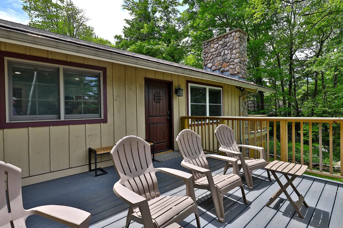 This image showcases a welcoming exterior view featuring a wooden deck with comfortable chairs, a prominent stone chimney, and the front door. The inviting setup suggests a place to relax outdoors after an evening out, encouraging socializing and connection with nature.