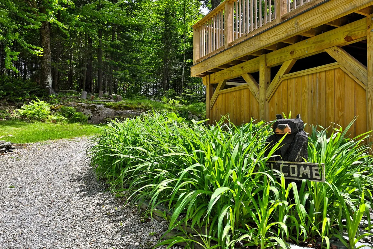 A wooden deck welcomes guests with a friendly bear sign, set against a backdrop of lush greenery. The deck suggests a transition space between indoor comforts and the regional outdoors, inviting relaxation after a day of exploring.