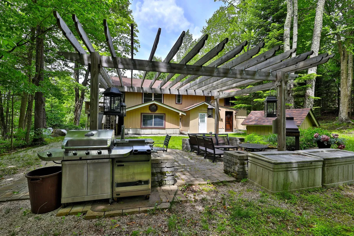 A well-appointed outdoor entertaining area with a grill, seating beneath a pergola, and abundant surrounding greenery. The space is perfect for group gatherings, alfresco dining, and social relaxation after a day of adventure.