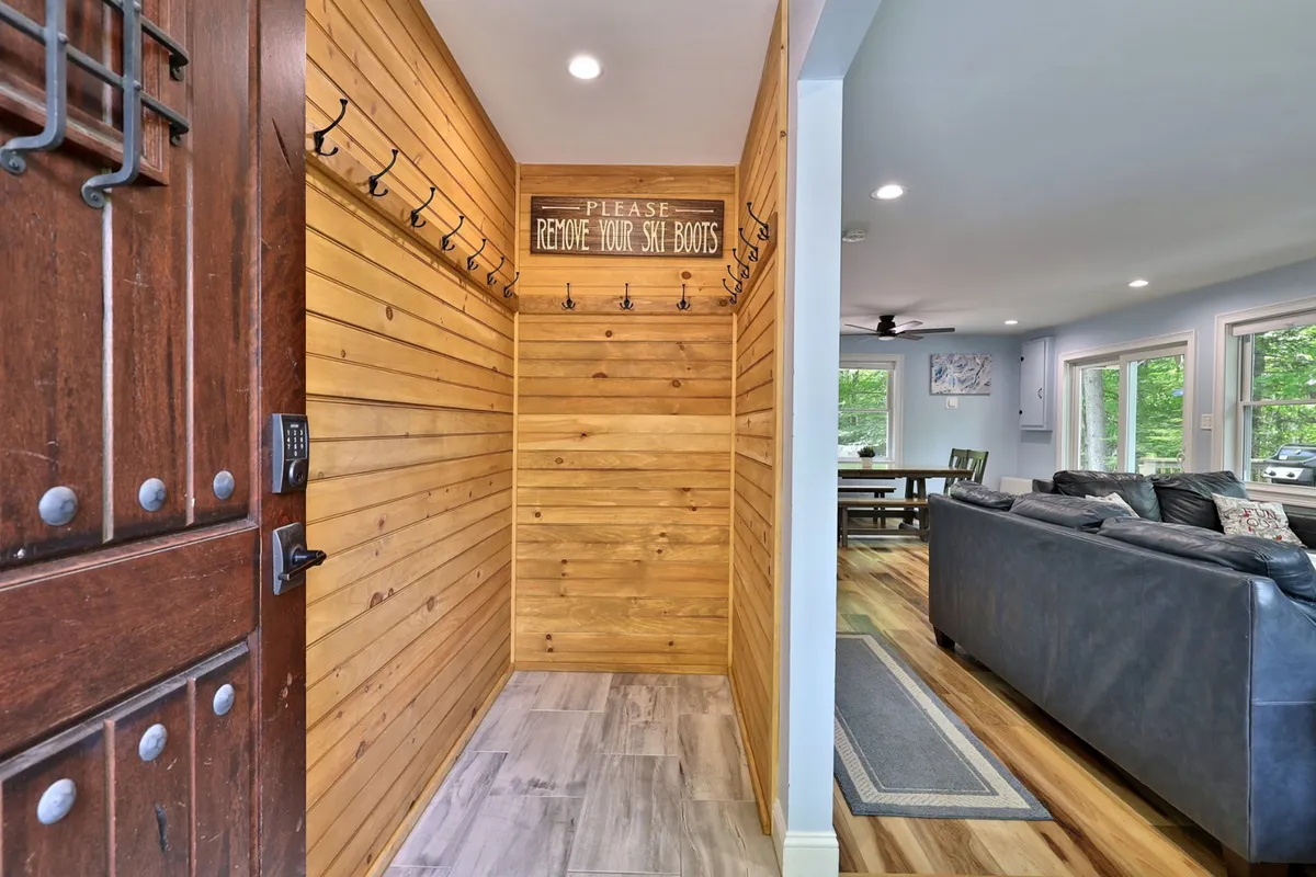 An inviting mudroom with wooden walls and door, coat hooks, and a removal sign. The area is ideal for organizing and transitioning from outdoor activities, such as skiing, to indoor comfort.