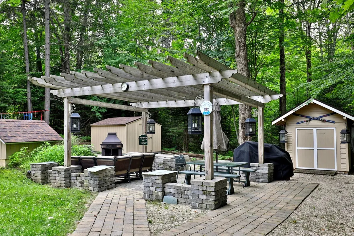 An exterior space showcasing a pergola, outdoor seating, a stone firepit, and a storage shed, all surrounded by greenery. The area invites social gatherings and relaxation after outdoor adventures.