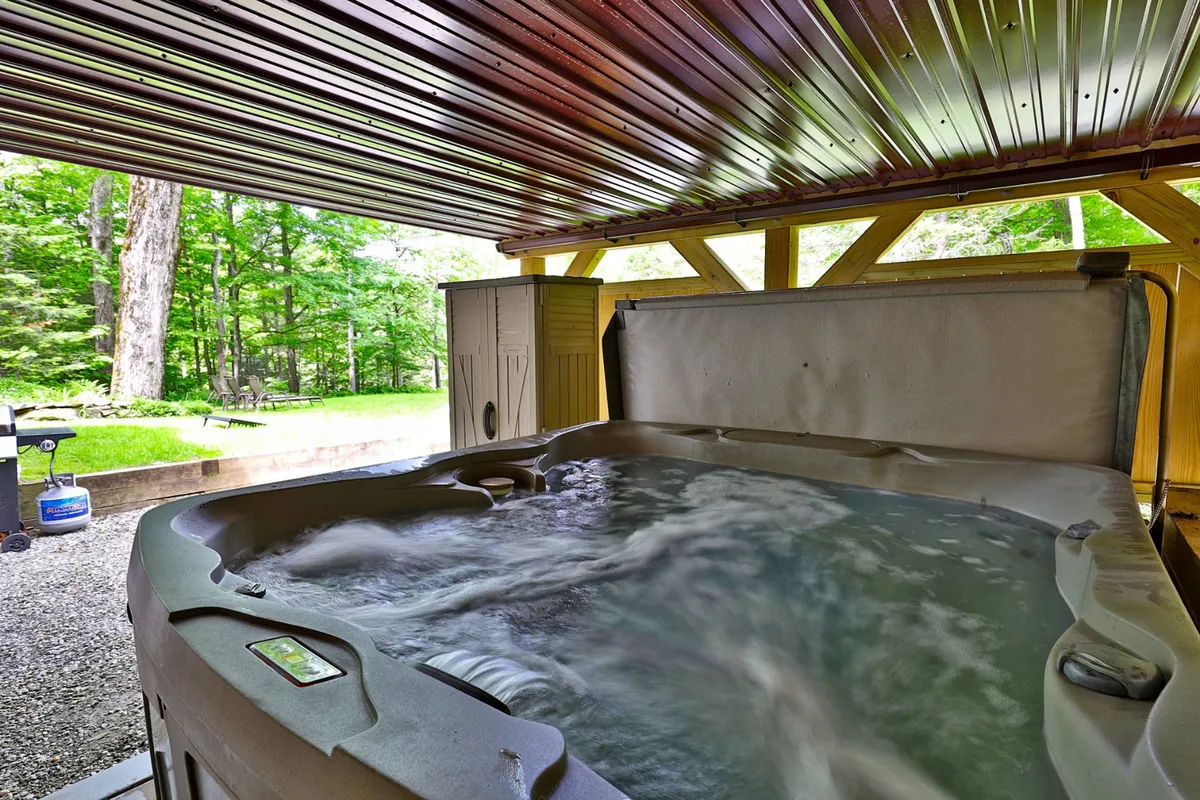 An inviting indoor hot tub set beneath rustic wooden beams, with large windows framing views of the surrounding landscape. The ambiance is tranquil, with natural light pouring in, and the space feels private and rejuvenating—perfect for unwinding after a day outdoors.